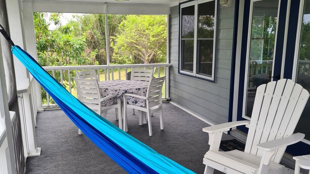 A covered porch with a table and chairs, a hammock, and a view of greenery. - Beautiful home with wifi, tv, A/C, private dock, & backup generator power (Hope Town, Abaco)