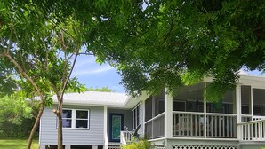 A two-story house with a front porch and a covered deck. - Beautiful home with wifi, tv, A/C, private dock, & backup generator power (Hope Town, Abaco)