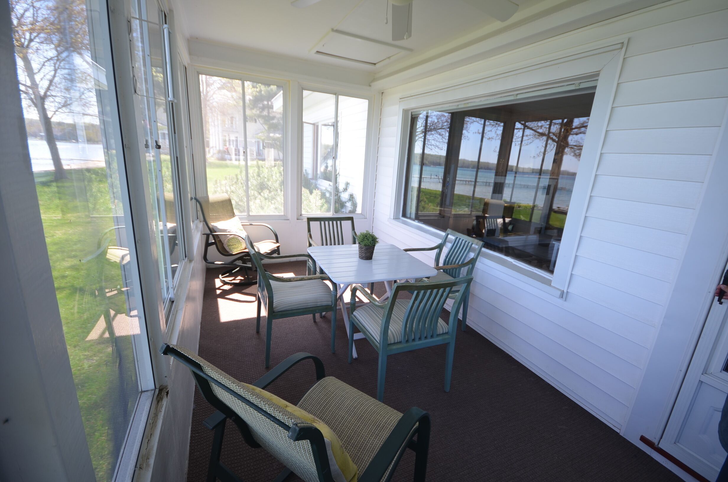 A covered patio with a table and chairs, large windows, and a view of a lake.