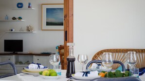 A dining table set with plates, glasses, and a bottle, with a wicker chair and a television in the background. - Apartment/ flat - Scicli (Donnalucata)