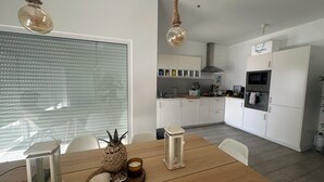A modern kitchen with white cabinets, a built-in oven, and a dining area with a wooden table. - The perfect oasis in Salema (Vila do Bispo)