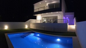Ett modernt hus i två våningar med en pool, fotograferat under natten.