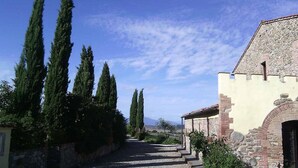 A stone building with a rustic entrance, a gravel pathway leading to it, and tall cypress trees lining the path. - Panorama, relax in farmhouse 30 kw from Volterra e 40 from Pisa airport (Chianni)