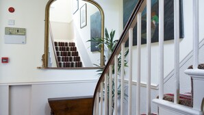 Eine Treppe mit weißer Geländer, eine Holzbank, ein Spiegel und ein an der Wand befestigter Rauchmelder.