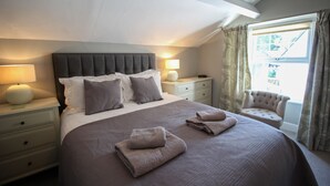 Une chambre à coucher avec un grand lit, deux tables de chevet, une chaise et une fenêtre avec des rideaux.
