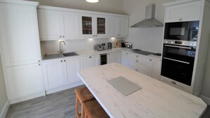 Une cuisine moderne avec des meubles blancs, un îlot en marbre et des appareils électroménagers intégrés, notamment une cuisinière et un four.