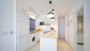 Una cucina moderna con mobili bianchi, forno integrato, microonde e lavatrice.