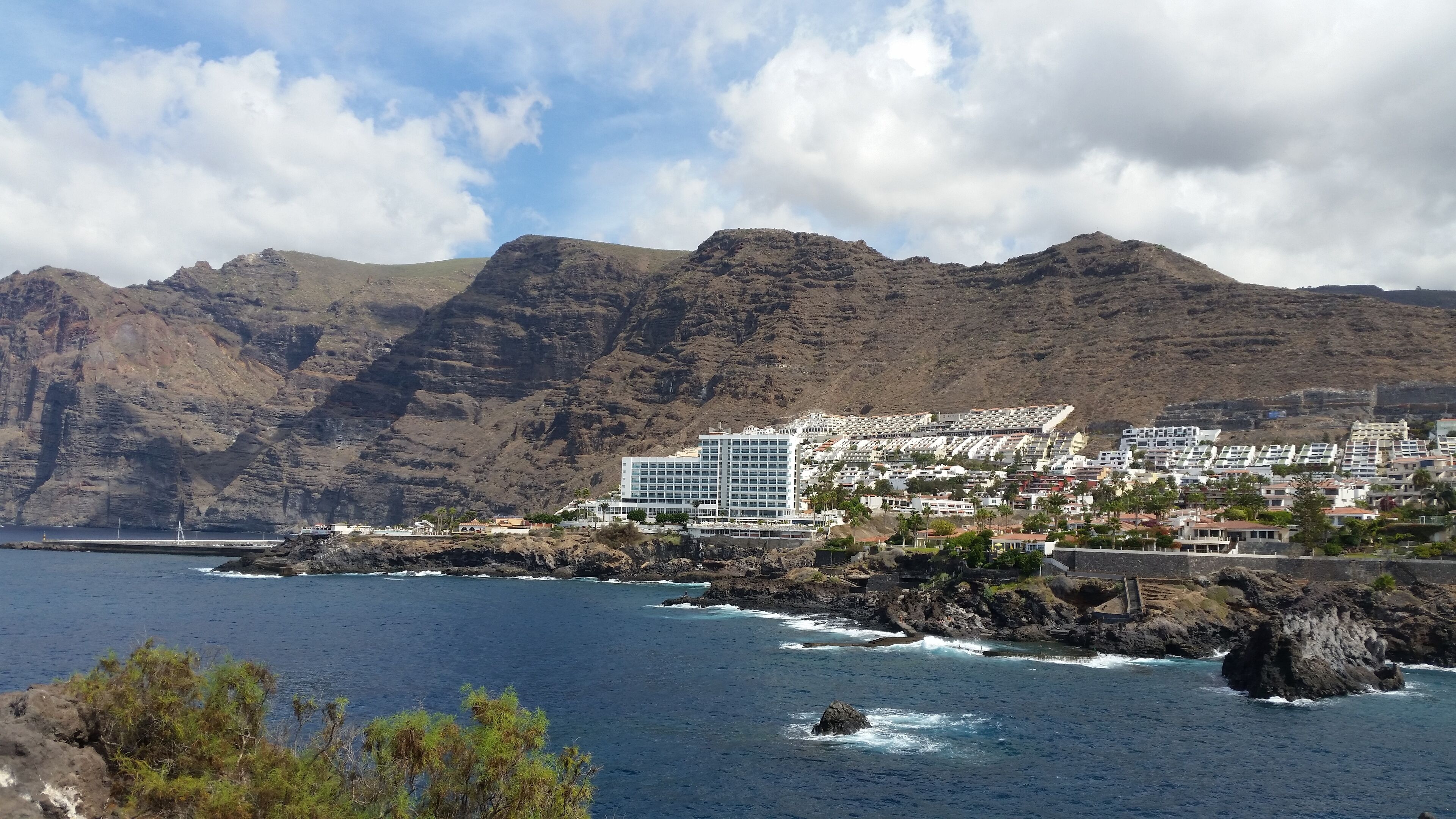 Ein Küstenhotel mit modernem Design, gelegen an einer felsigen Küste mit Blick auf das Meer und Berge im Hintergrund.