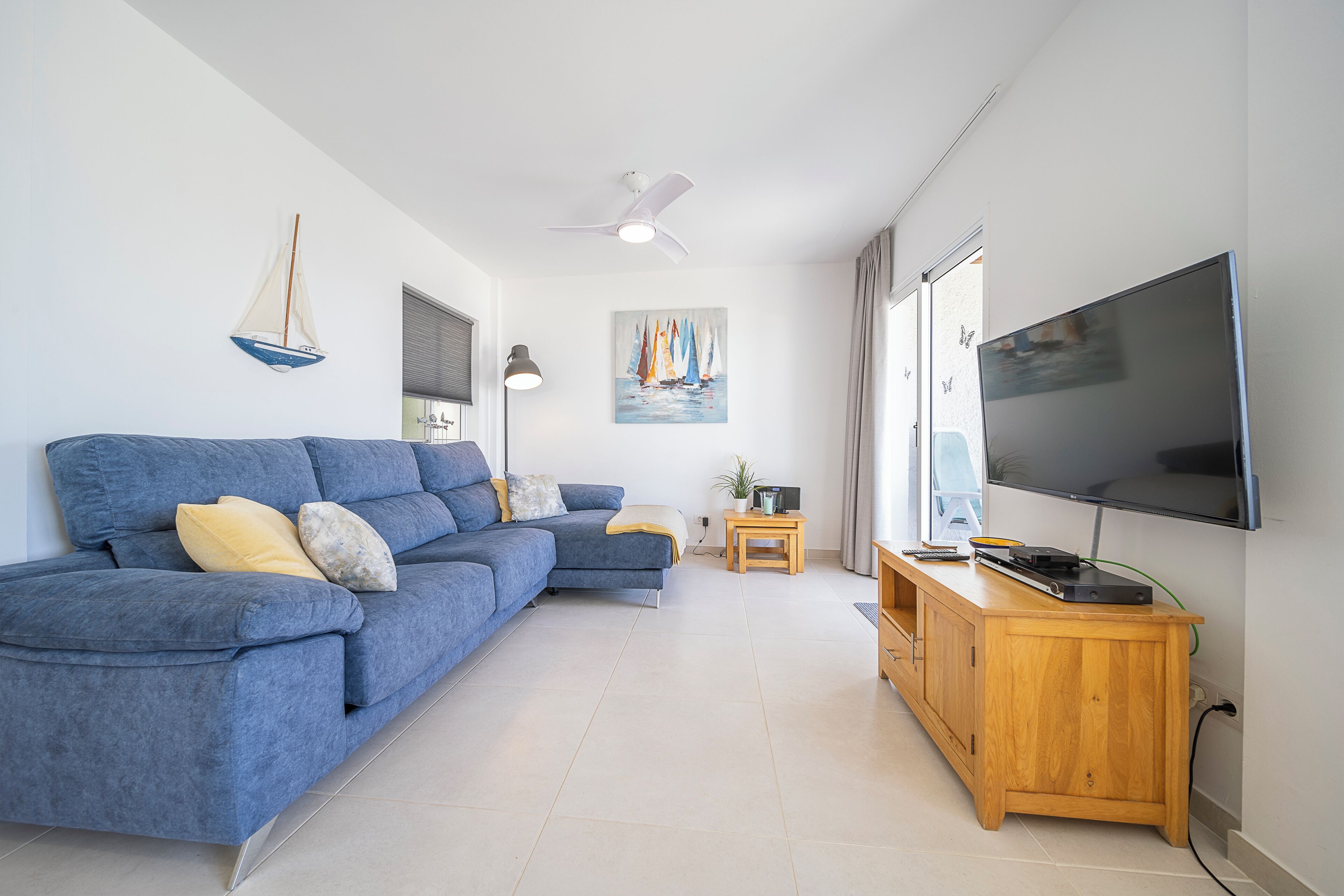 A modern living room with a blue sectional sofa, a wooden TV stand, and a ceiling fan.