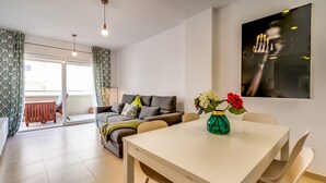 A modern living room with a sofa, a dining table, and a vase with flowers. - Apt. with 4 pools, very close to Fenals beach, 6 pax, air conditioning and free wifi. (Lloret de Mar)