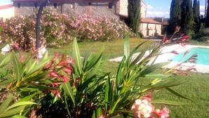 Una piscina envoltada d'un jardí ben cuidat amb plantes en flor i un edifici de pedra al fons.