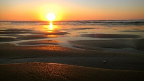 Ein Sonnenuntergang über einem Strand, das feuchte Sand reflektiert das Licht.