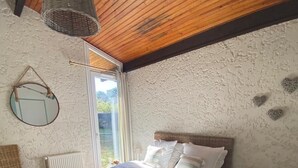 Ein Schlafzimmer mit einem Bett, einem Sessel, einem Nachttisch, einer Lampe, einer Pendelleuchte und einem Fenster.
