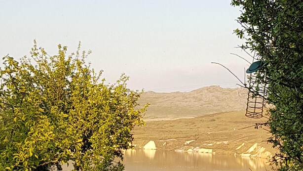 A table with a bottle of wine and a glass, set against a scenic backdrop of a lake and hills. - Stunning uninterrupted moorland views over lake and Rough Tor (Advent)