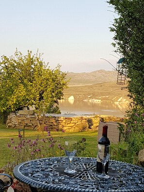 Une table avec une bouteille de vin et un verre, placée devant un paysage pittoresque composé d’un lac et de collines.