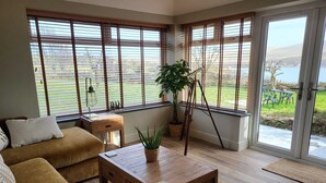 A living room with a sofa, a wooden coffee table, and a view of a lake through large windows. - Stunning uninterrupted moorland views over lake and Rough Tor (Advent)