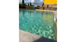 En klar swimmingpool med stenkant og en gul bygning i baggrunden.