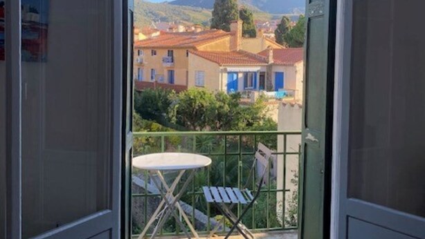 Ein Balkon mit Tisch und Stühlen mit Blick auf eine Stadt, mit Gebäuden und Bergen im Hintergrund.