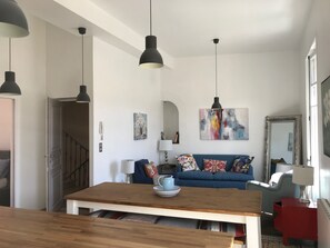 A modern living room with a wooden dining table, blue sofa, and artwork on the walls.