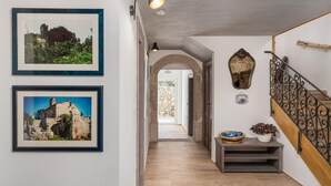 A hallway with framed pictures, a stone wall, a staircase with wrought iron railings, and a small table with a plant. - Awesome home in Kornic (Kornic)