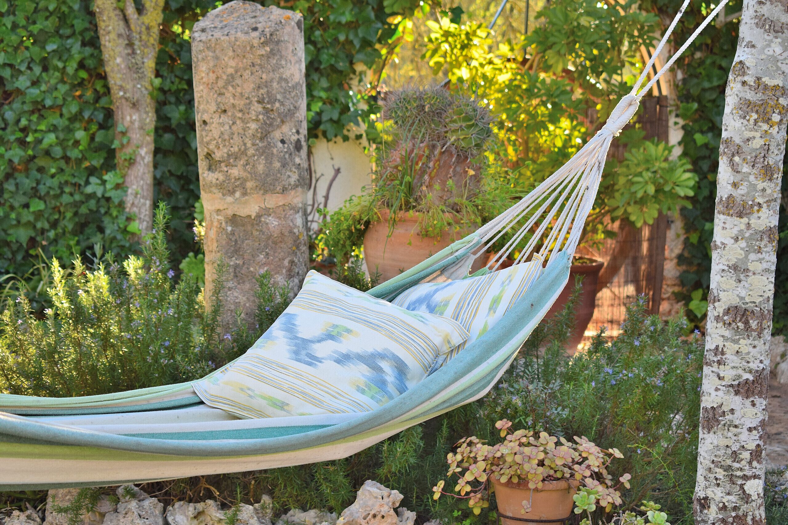 A hammock in a garden setting with stone structures and potted plants.