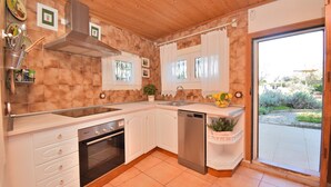 Une cuisine avec des meubles blancs, une hotte de cuisinière en acier inoxydable, un lave-vaisselle et une fenêtre avec des rideaux.