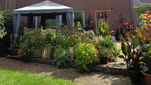 A two-story house with a brick exterior, a satellite dish, and a covered patio area with potted plants and flowers. - Modern, exclusive and bright apartment in Rees (Rees)