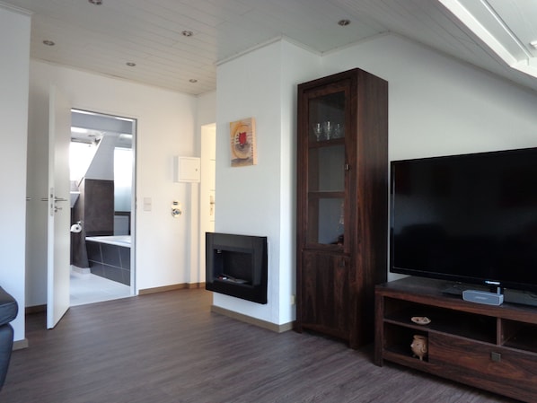 A modern living room with a flat-screen TV, wooden cabinet, and fireplace.