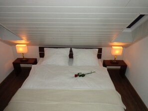 A neatly made bed with white linens, two bedside lamps, and a single rose on the bed.