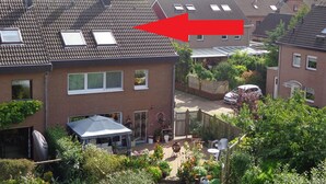 A residential area with houses, a garden, and a red arrow pointing to a house with a tiled roof and skylights. - Modern, exclusive and bright apartment in Rees (Rees)