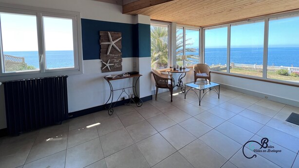 A spacious room with a view of the sea, a wooden ceiling, and a table with chairs.