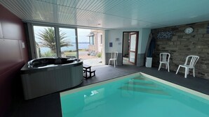 A swimming pool area with a hot tub, chairs, and a view of the sea.