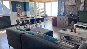 A spacious living area with a sofa, dining table, and chairs. There is a fireplace with a stone wall and a television.