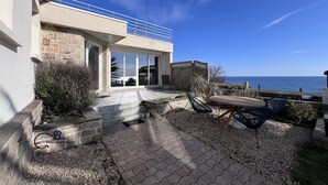 A modern house with a patio, outdoor seating, and a view of the sea.