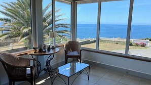 A room with a view of the sea, a wicker chair, a glass table, and a lamp.
