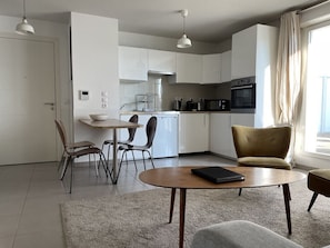 Une cuisine moderne avec des meubles blancs, un coin repas doté d’une table ronde et un canapé.