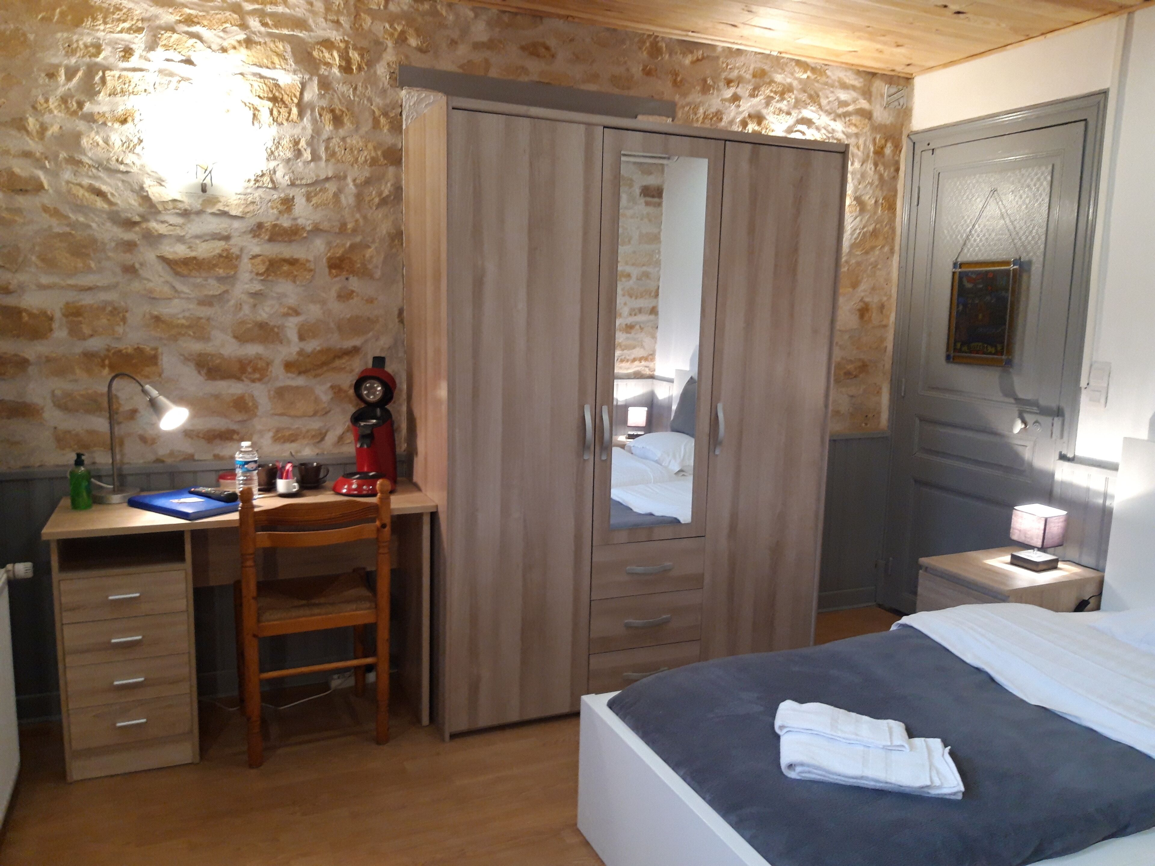 Un dormitorio con cama, escritorio y silla, armario y mesita de noche con lámpara.