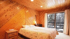 A cozy bedroom with a wooden sloped ceiling, a bed with floral bedding, a nightstand, and a window with a view of a snowy landscape. - 61 Jabberwocky Private vacation home 5 bedroom, pet friendly clubhouse amenities (Fraser)