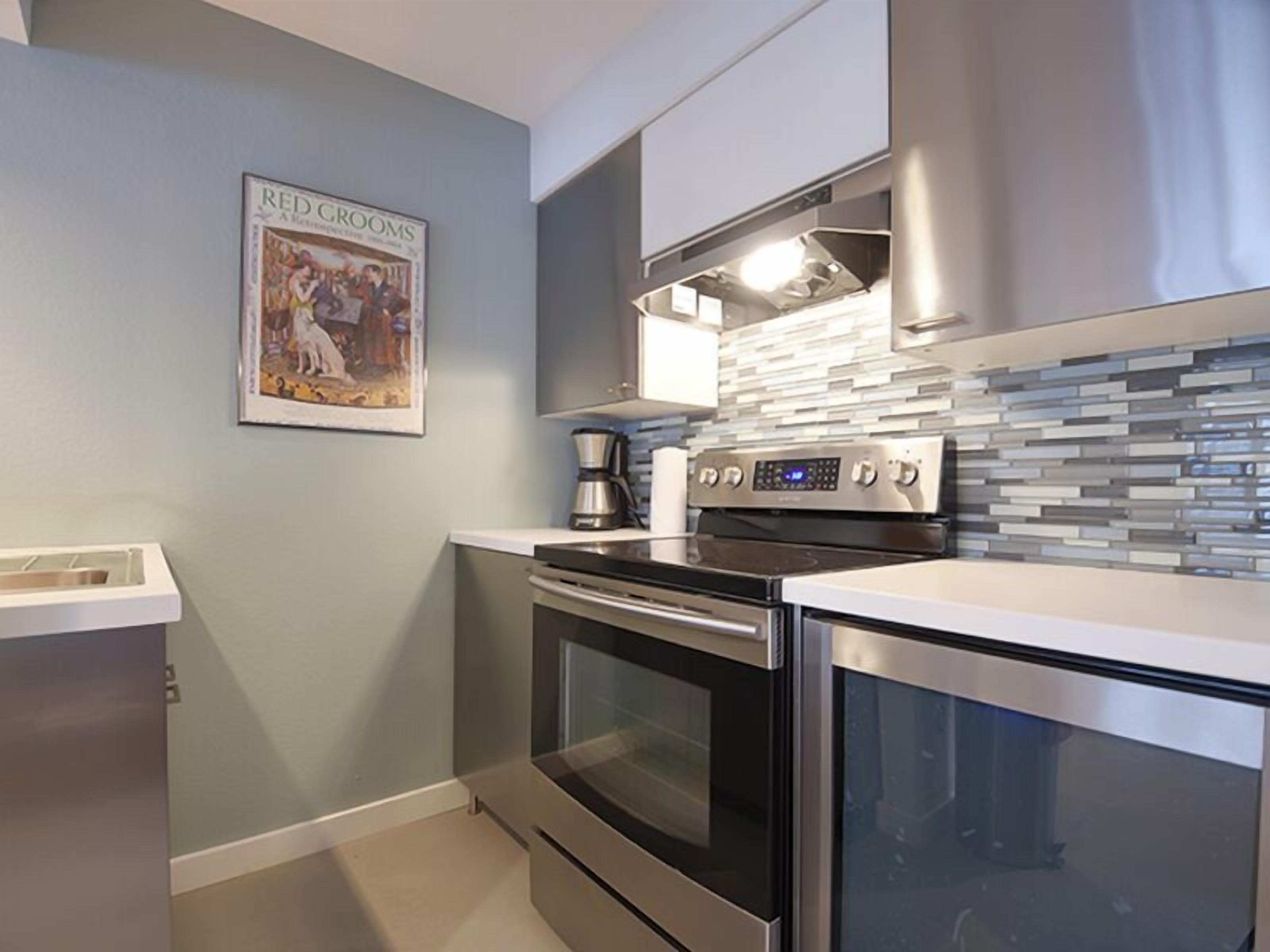 A modern kitchen with stainless steel appliances, a tiled backsplash, and a framed picture on the wall.