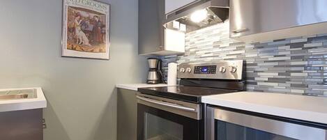 A modern kitchen with stainless steel appliances, a tiled backsplash, and a framed picture on the wall.