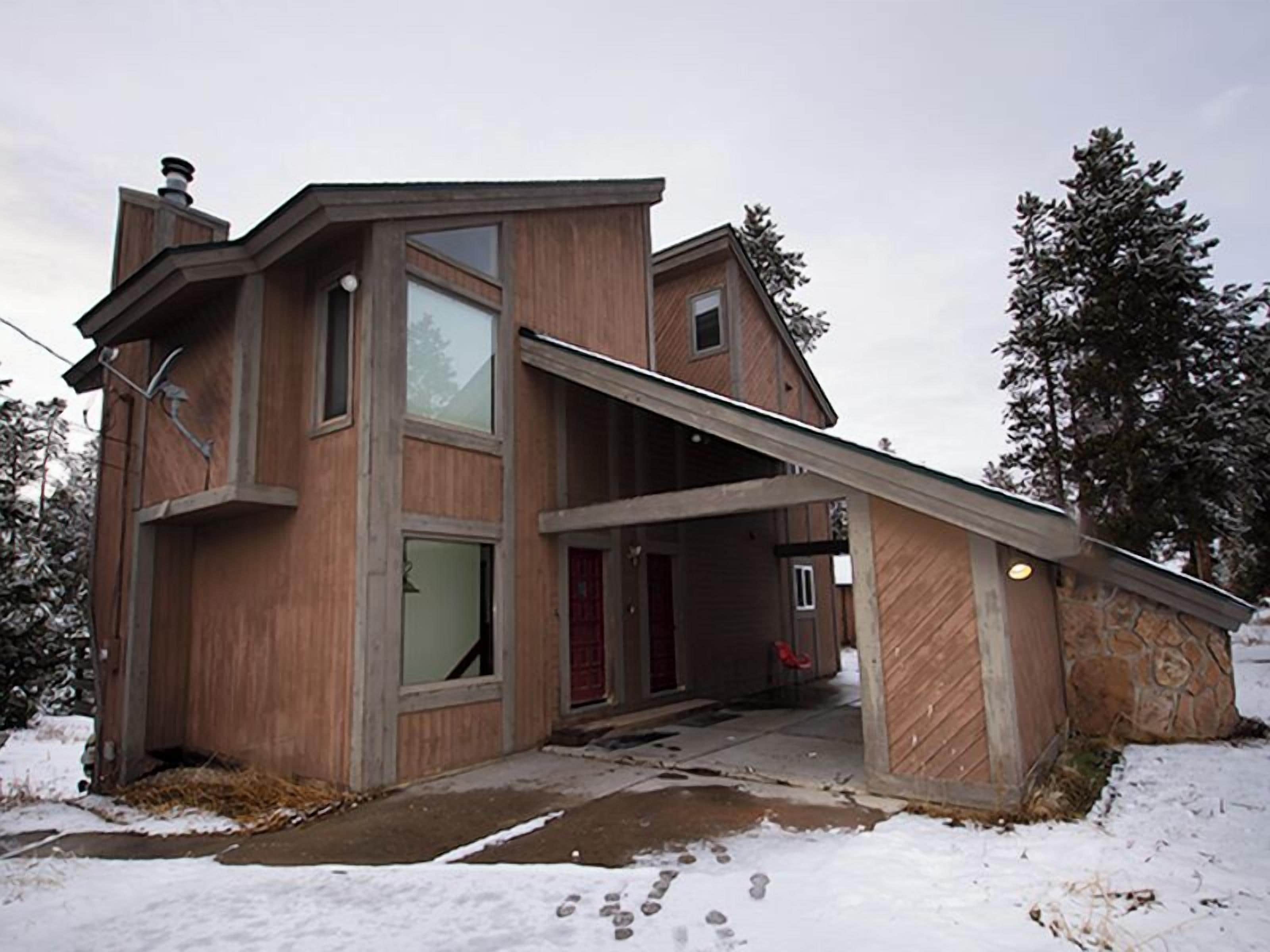 A two-story house with a steeply pitched roof, large windows, and a visible chimney.