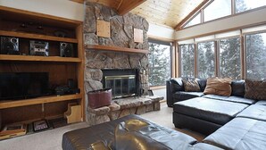 A cozy living room with a stone fireplace, wooden shelves, a leather sofa, and large windows offering a view of trees. - 61 Jabberwocky Private vacation home 5 bedroom, pet friendly clubhouse amenities (Fraser)