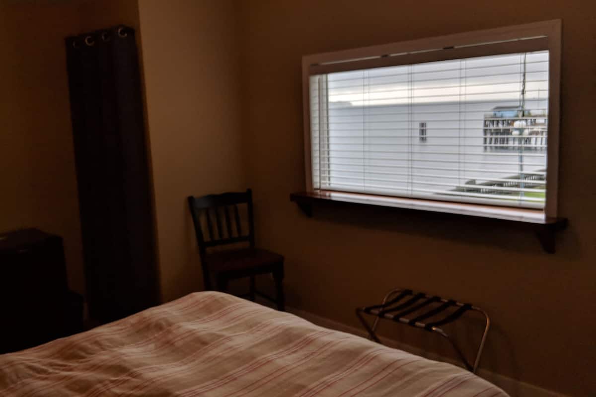 A bedroom with a bed, a chair, a radiator, a window with blinds, and a curtain.