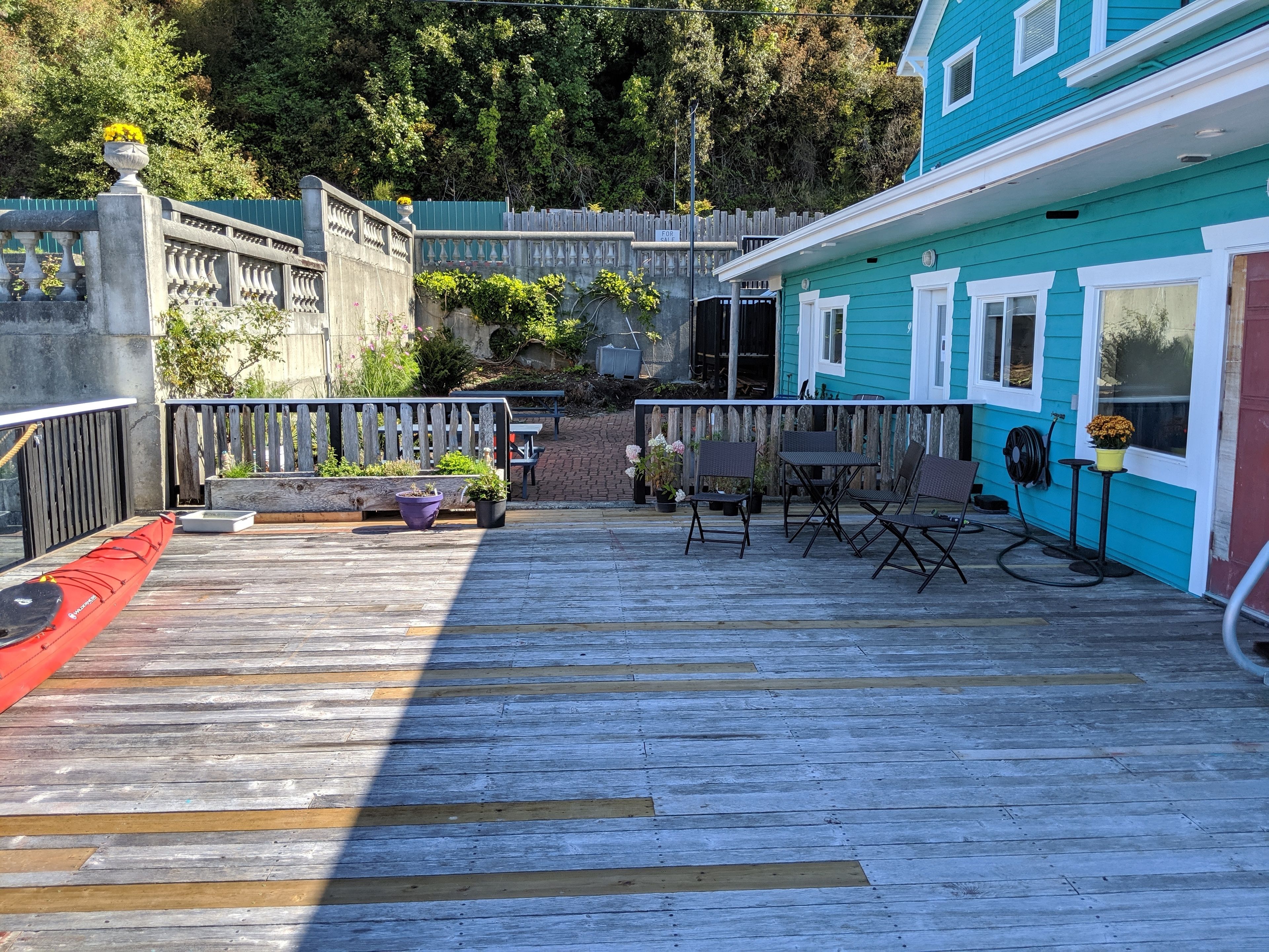 A wooden deck with outdoor seating, a kayak, and a house with teal siding.