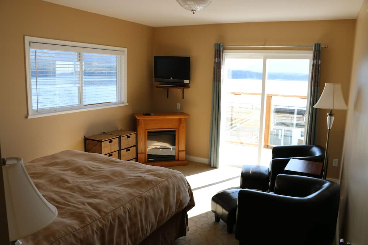 A bedroom with a bed, a television, a fireplace, a chair, and a view through a window.