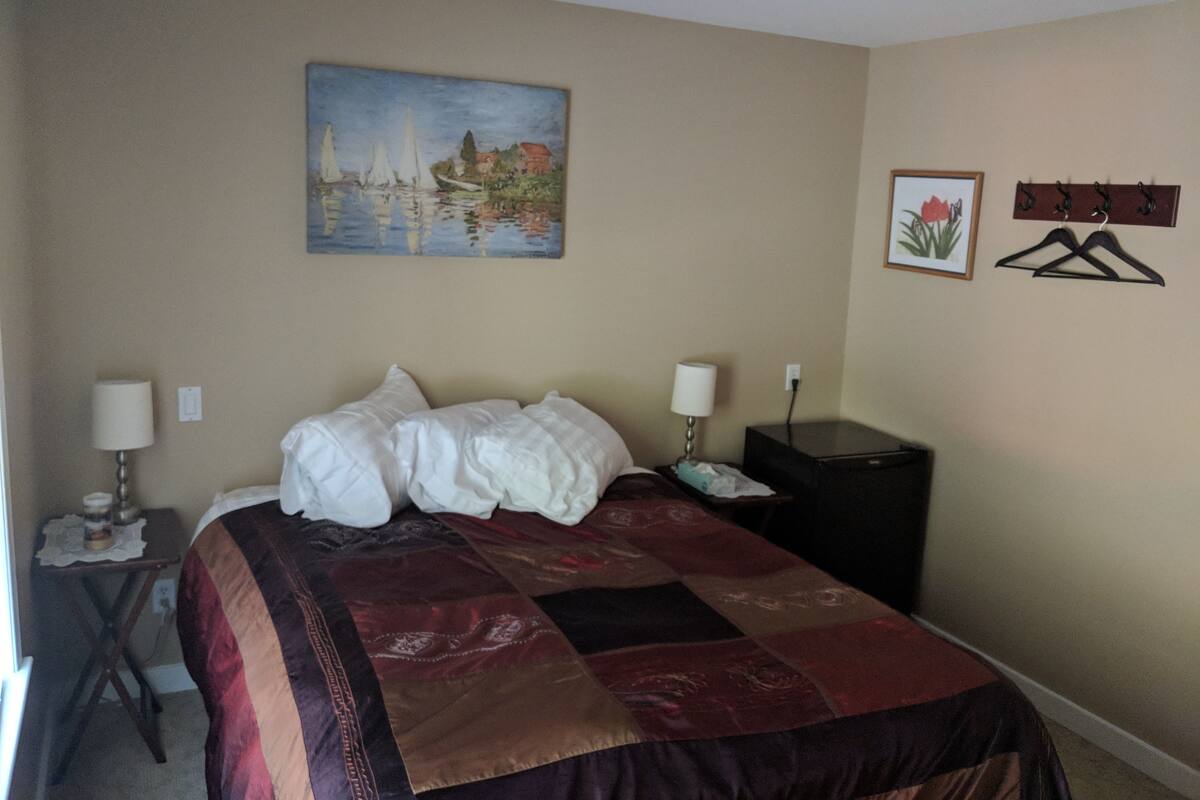 A hotel room with a bed, two bedside tables, a painting on the wall, and a coat rack.