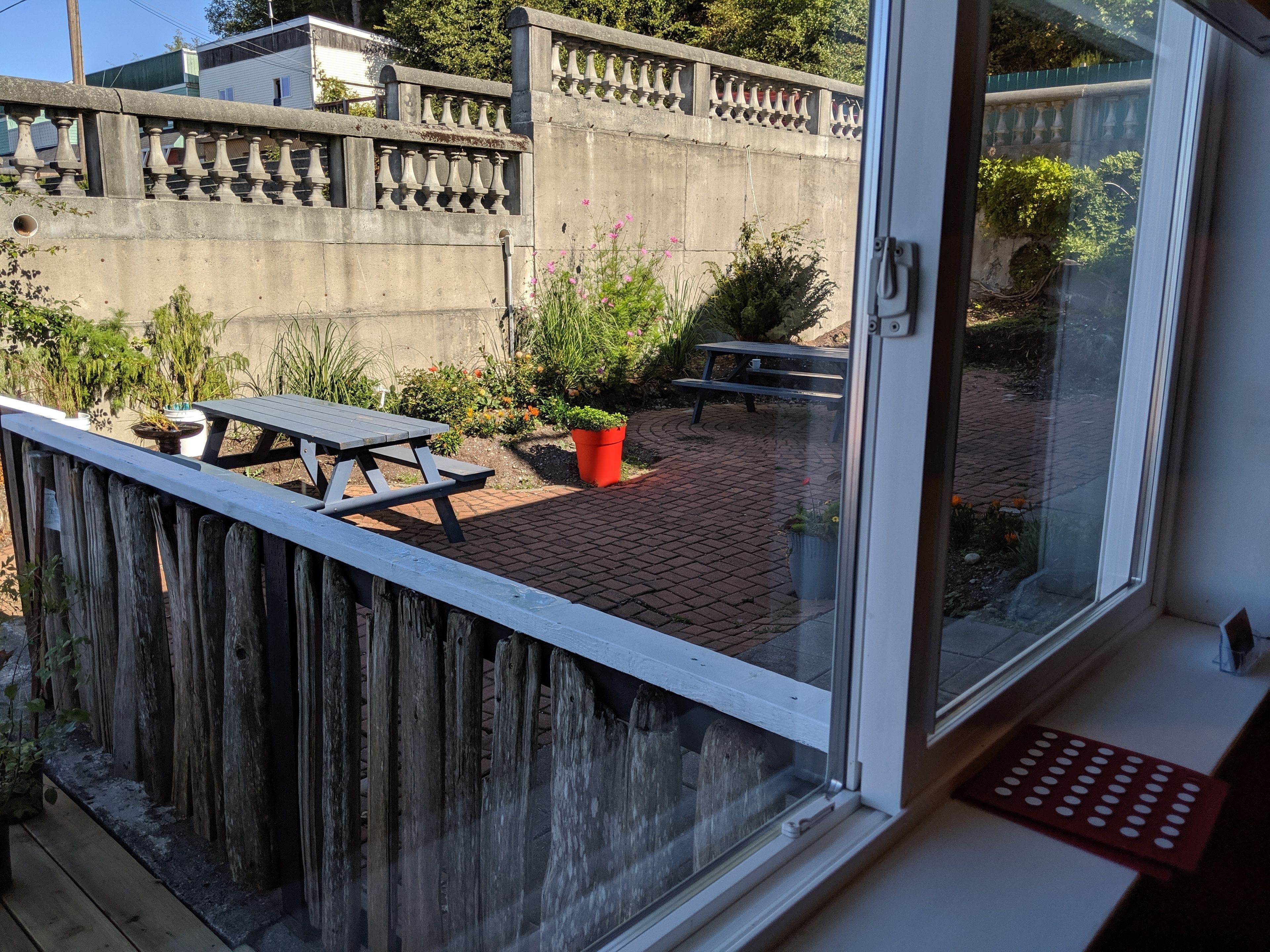 Une terrasse en bois avec une table de pique-nique et un pot de fleurs rouge.
