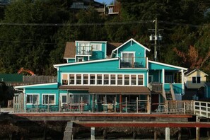 A turquoise two-story building with a balcony, a covered front porch, and a wooden deck.