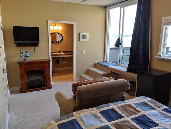 A hotel room with a bed, a television, a fireplace, a window with curtains, and a view of the outside.