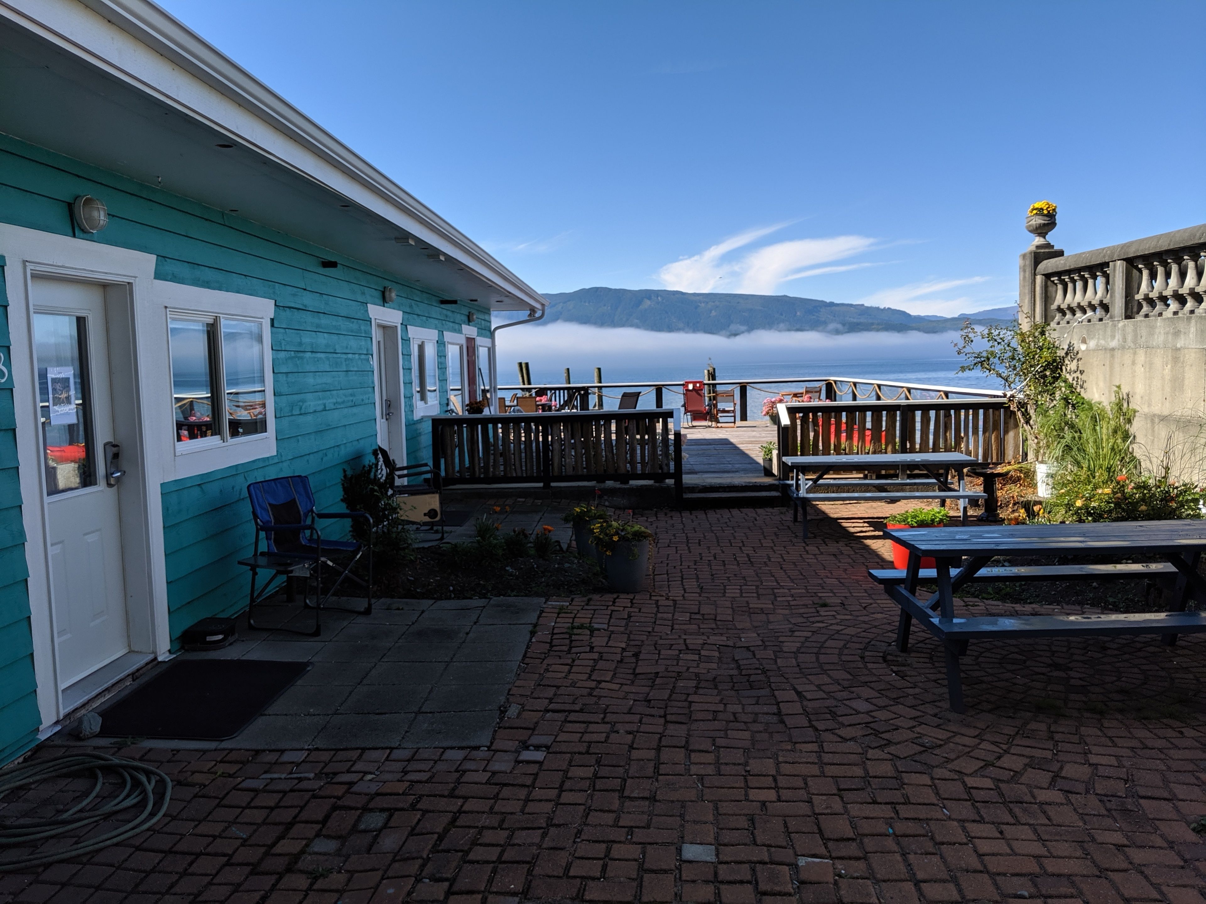 Een turquoise gebouw met een houten terras, buiten zitplaatsen en uitzicht op zee.